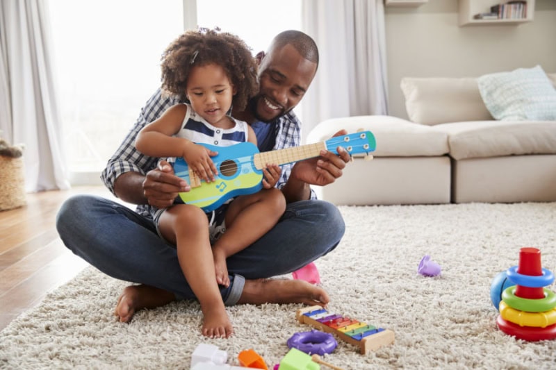 Dad and toddler sitting on living room floor.