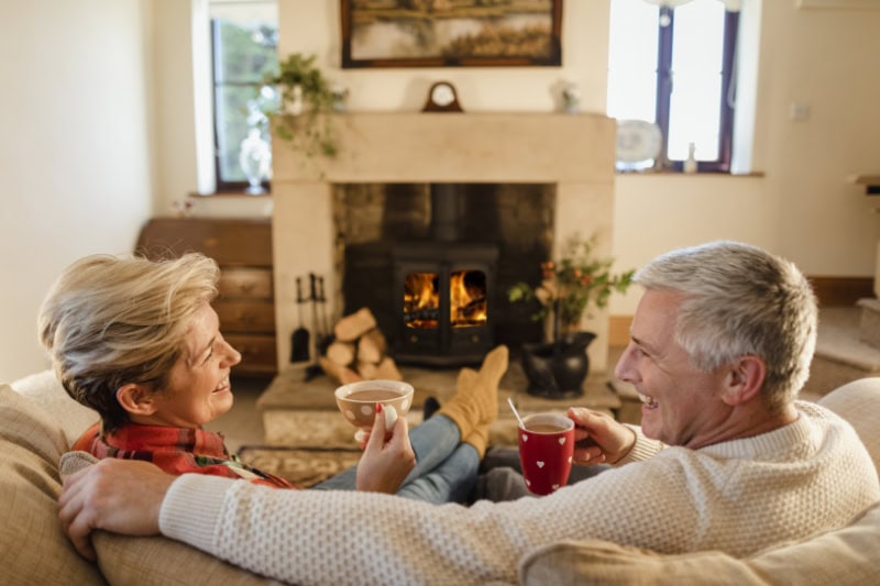 Husband and wife relaxing on couch in front of fire.