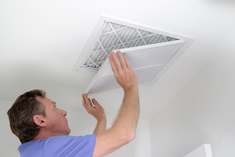 HVAC technician changing filter in home.