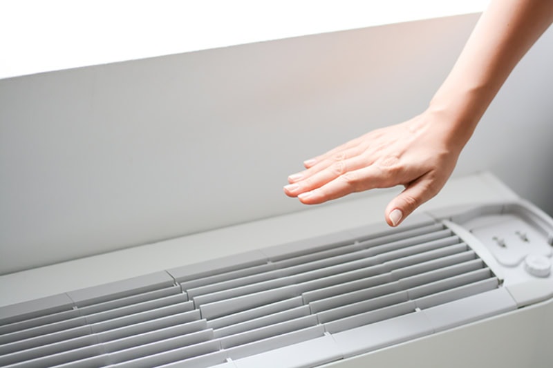 a hand hovering over the vent of an air conditioning system.